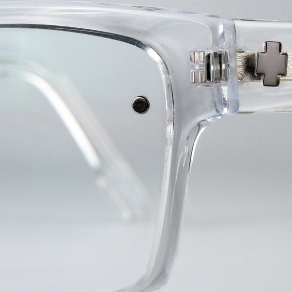 Close-up of clear eyeglasses with a metallic hinge and Chemistrie magnets on a light gray background