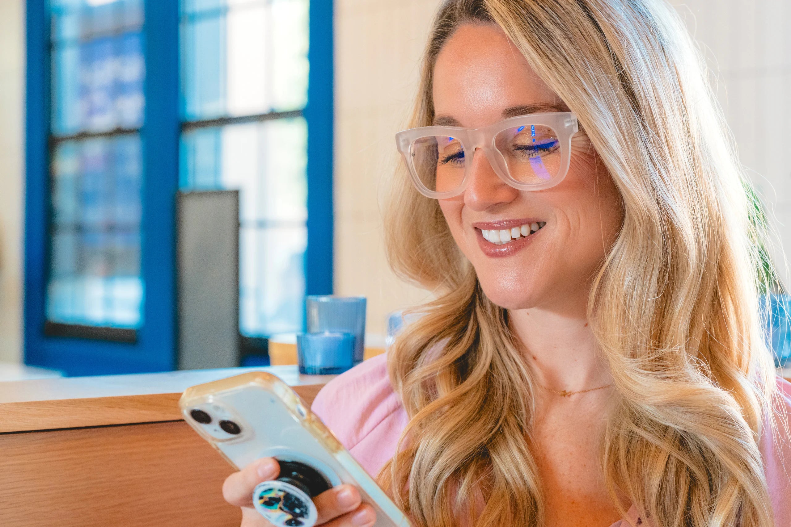 A woman at a desk holding a phone, wearing clear eyeglasses