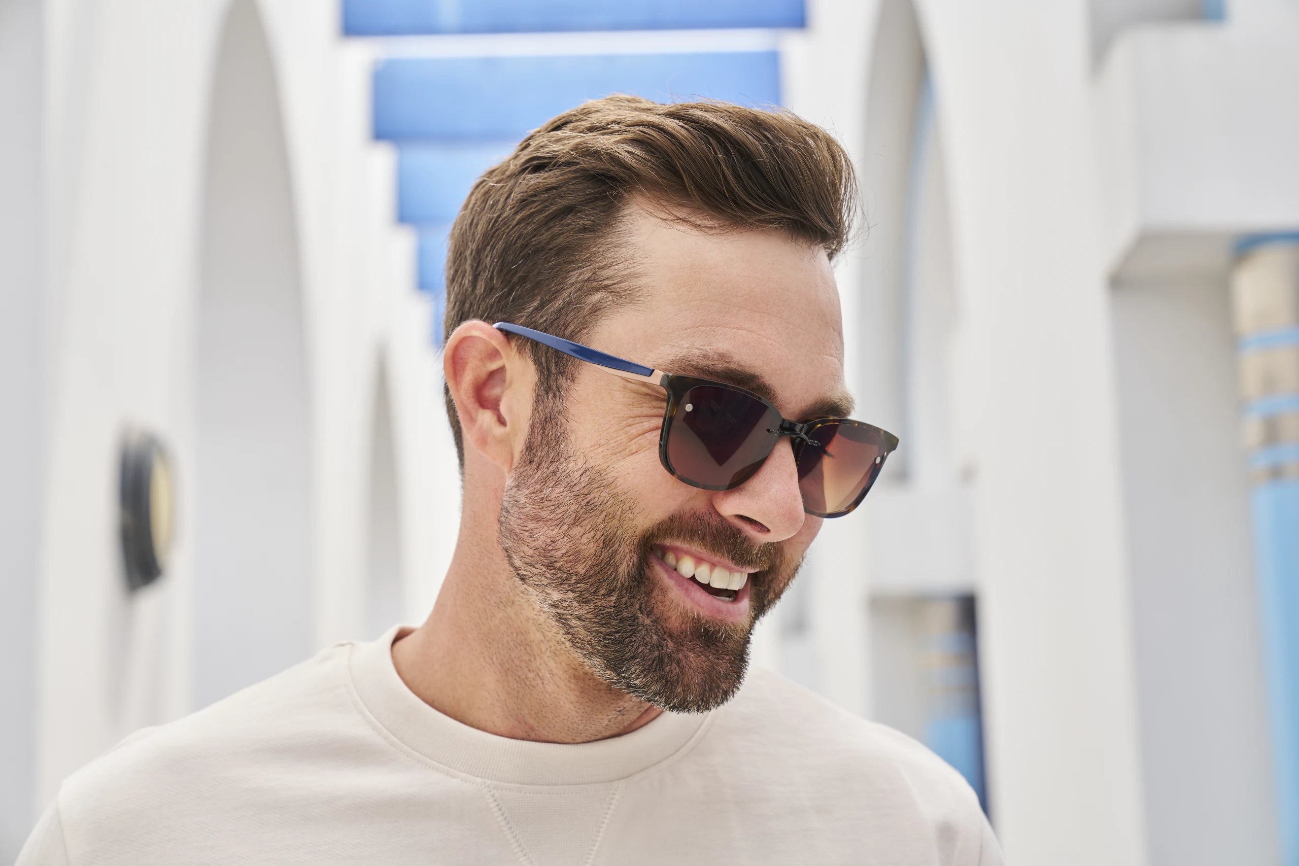 A man in a cream sweater outdoors in glasses fitted with a dark clip