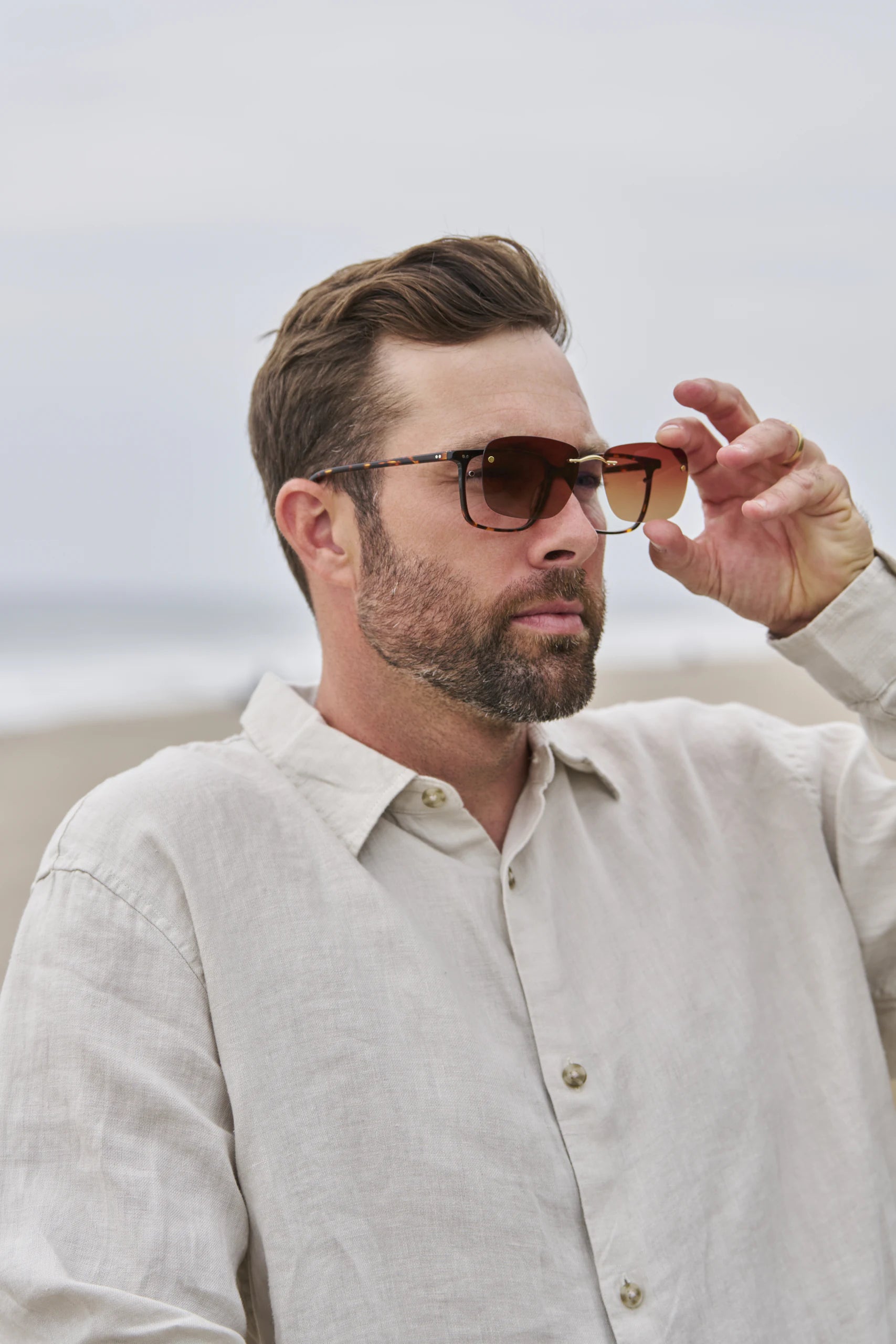 A man by the sea lifting a clip away from his eyeglasses