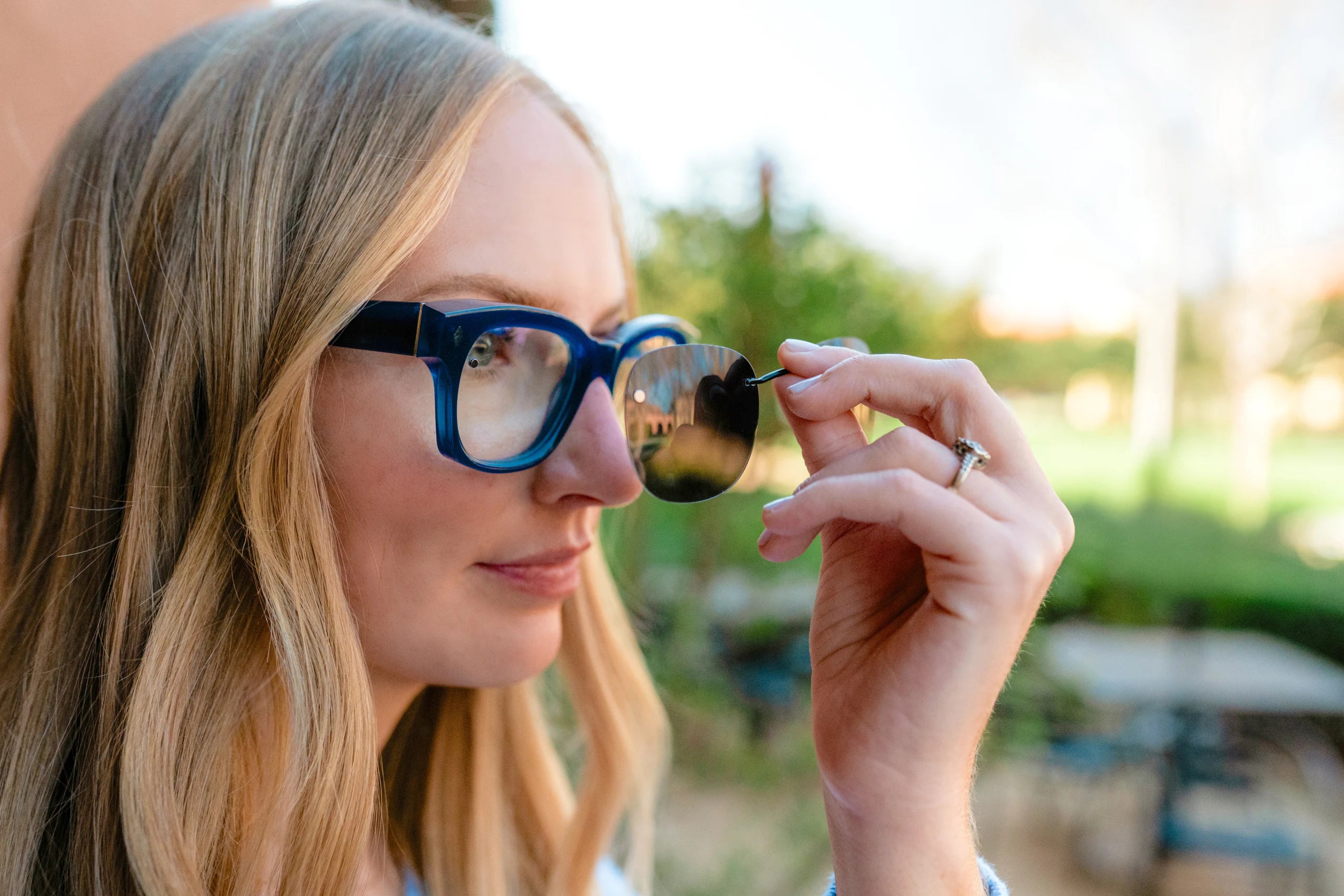 A woman lifting a sun clip away from her blue eyeglasses