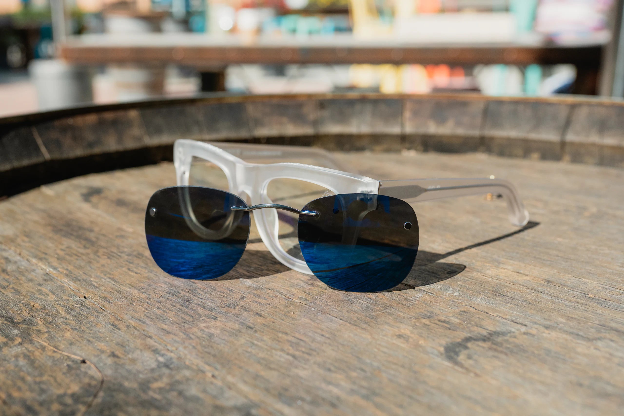A pair of clear eyeglasses with a blue mirrored clip resting on wood