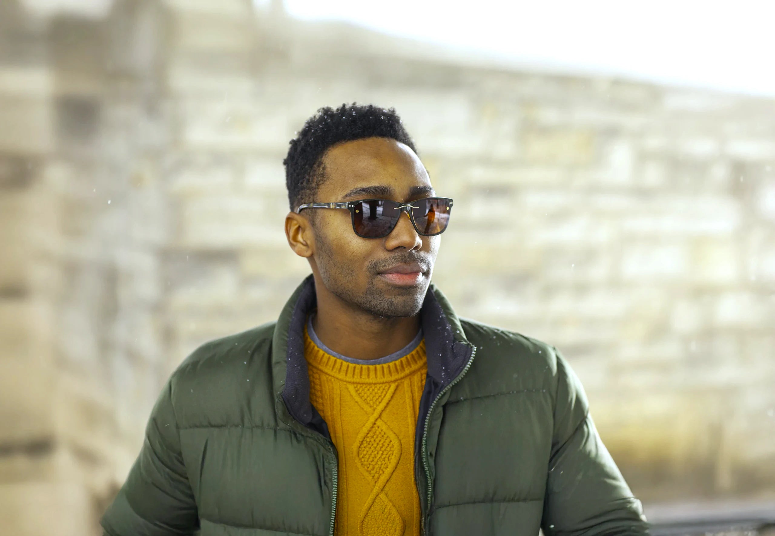 A man in a green jacket outdoors in glasses fitted with a dark clip